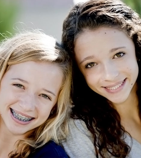 Two smiling girls with braces posing outdoors in natural daylight.