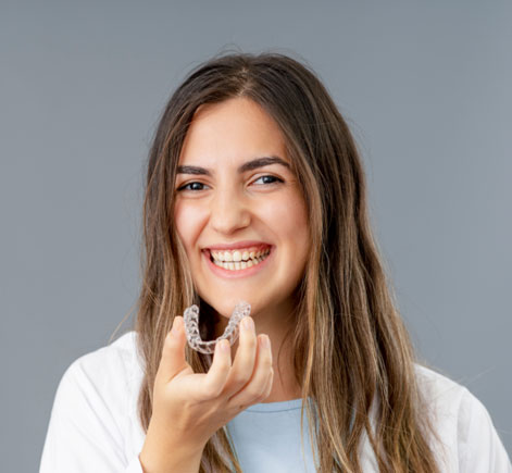 Woman smiling while holding dental floss, gray background, dental care promotion.