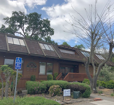 Brick dental office building with signage, landscaping, and blue umbrella near entrance.