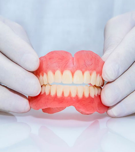 Dentist holding pink full dentures showing teeth alignment and fit in clinical setting.