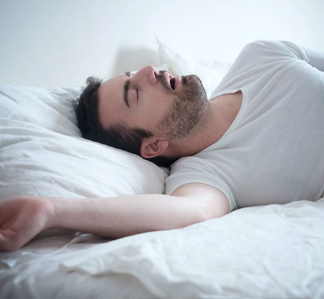 Man sleeping peacefully in bed with white bedding and pillow.