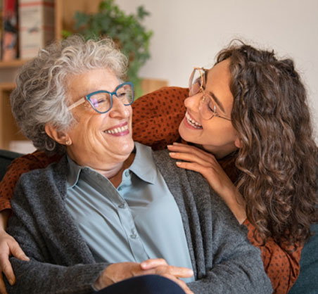 Older woman with gray hair and younger woman smiling together indoors, representing dental care family relationships.
