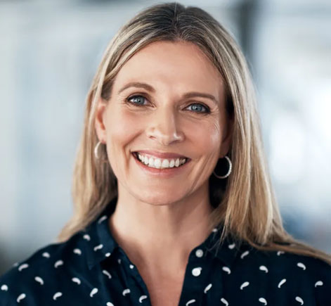 Professional woman smiling at camera, wearing dark patterned blouse in modern office setting.