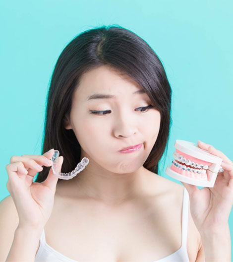 Young woman holding dental aligners against turquoise background, examining orthodontic treatment options.