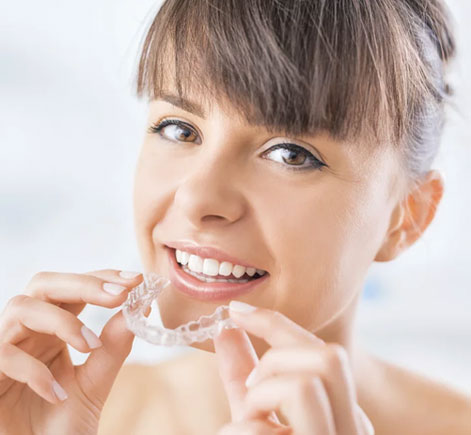 Young woman smiling while holding clear orthodontic aligners against white background.