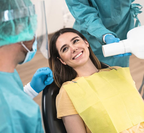 Woman in yellow shirt smiling during dental examination in dentist's office with healthcare provider.