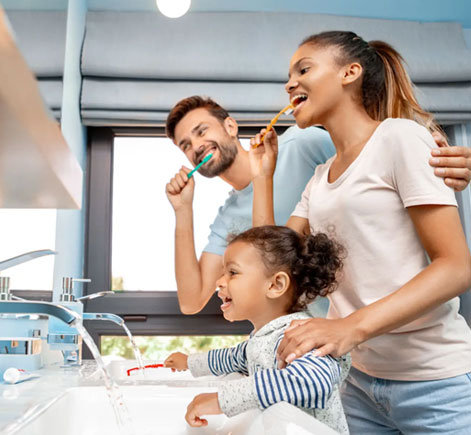 Family brushing teeth together in modern bathroom with mother, father, and young daughter.