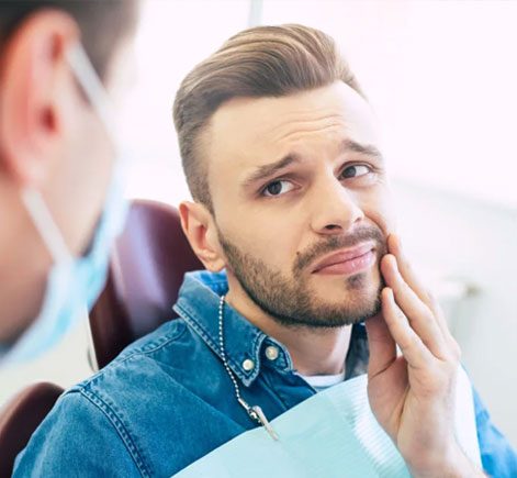 Man touching his face in dental office, examining teeth or jaw discomfort with dentist present.