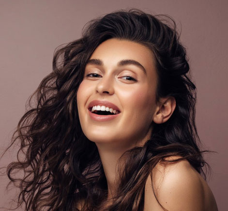 Woman smiling brightly against neutral background, professional headshot style portrait.
