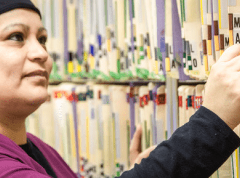 Dental professional organizing patient records on library shelves in clinical office setting.