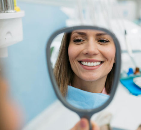 Woman smiling at reflection in mirror at dental office visit