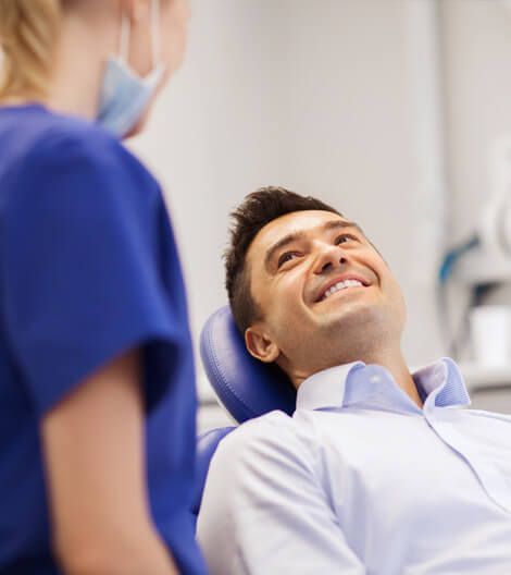 Male patient smiling in dental chair with female dentist in blue scrubs during examination.