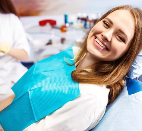 Young woman smiling in dental chair wearing blue bib during routine checkup at dentist office.