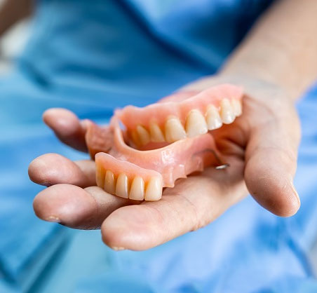 Hand holding two dentures against blue background in dental care setting