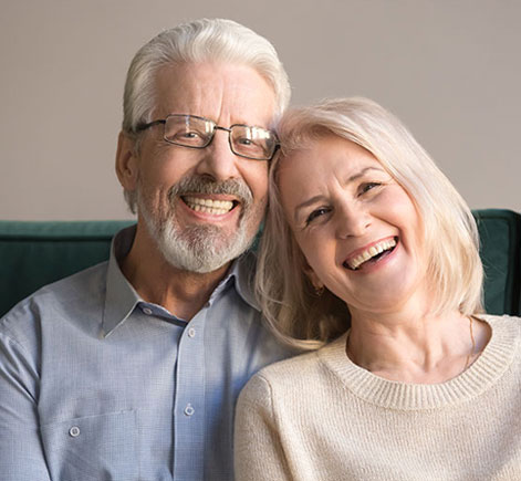 Happy mature couple smiling together on green couch in dental office setting.
