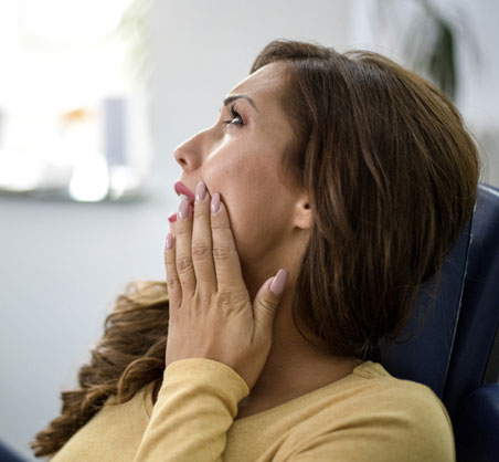 Woman in yellow shirt touching face in pain, dental office setting.