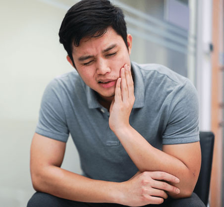 Man holding his cheek in discomfort, suggesting dental pain or toothache in an office setting.