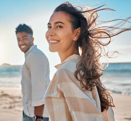 Happy couple enjoying beach sunset together, woman smiling at camera with windblown hair.