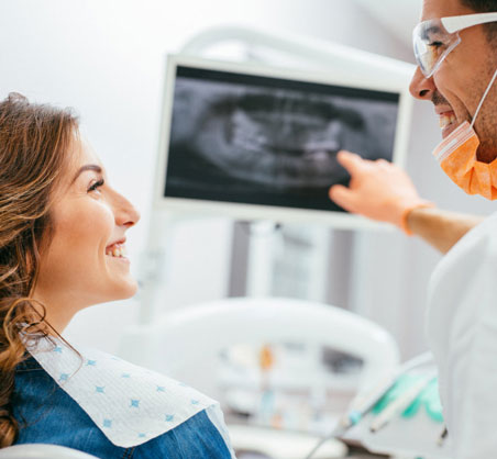 Dentist explaining X-ray results to smiling female patient in modern dental office.
