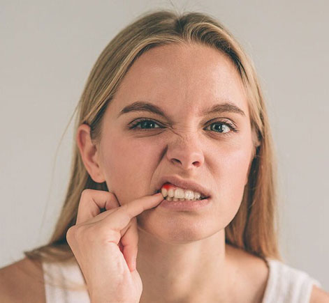 Woman with concerned expression touching her cheek, suggesting dental pain or discomfort in neutral indoor setting.