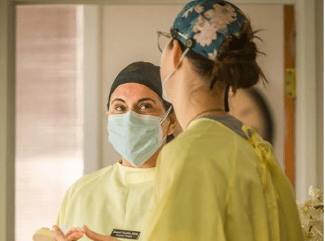 Dental professional wearing mask and headlamp examines patient in clinical treatment room.